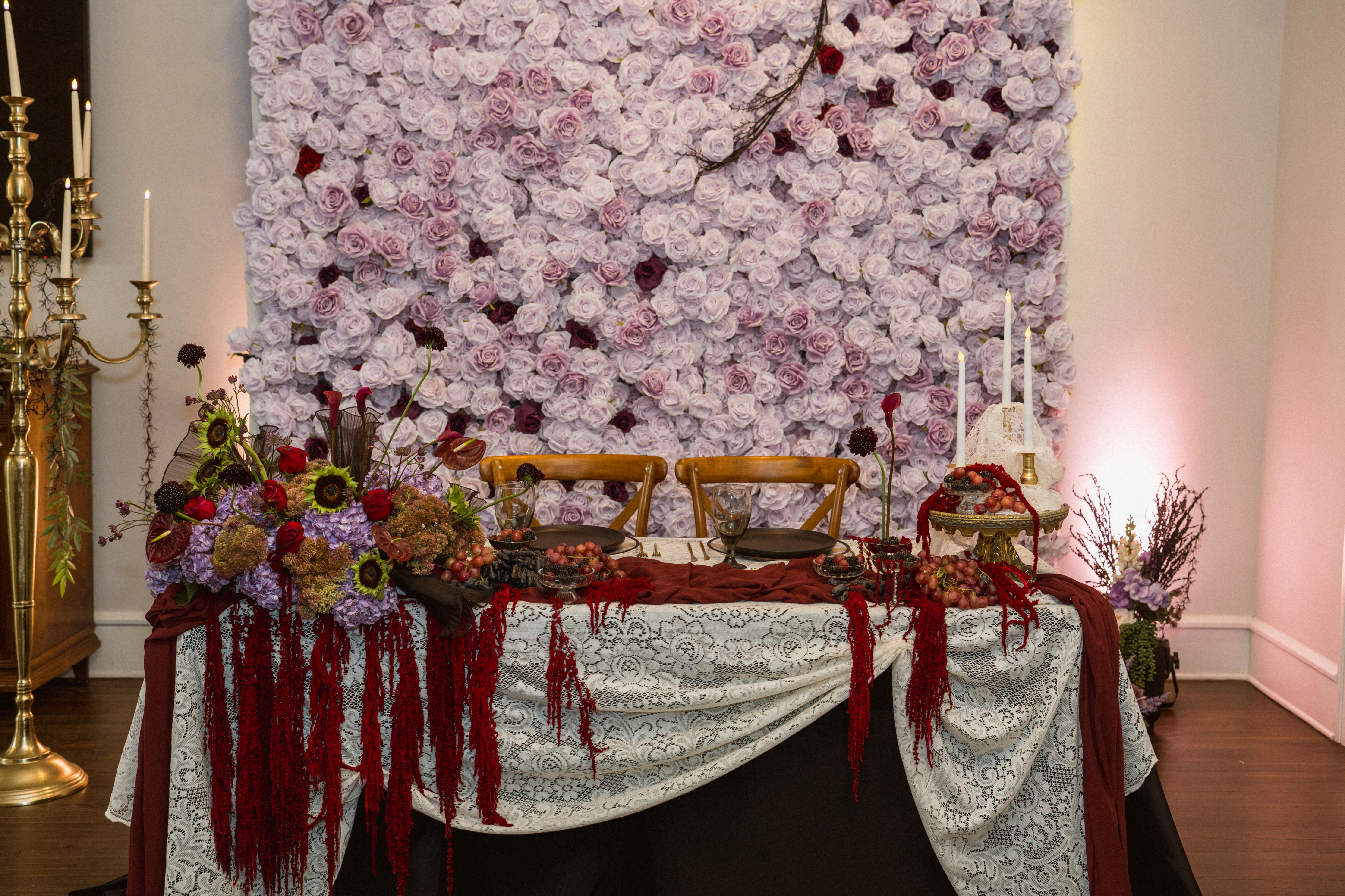 Lilac rose flower wall behind a sweetheart table styled with burgundy florals and candles